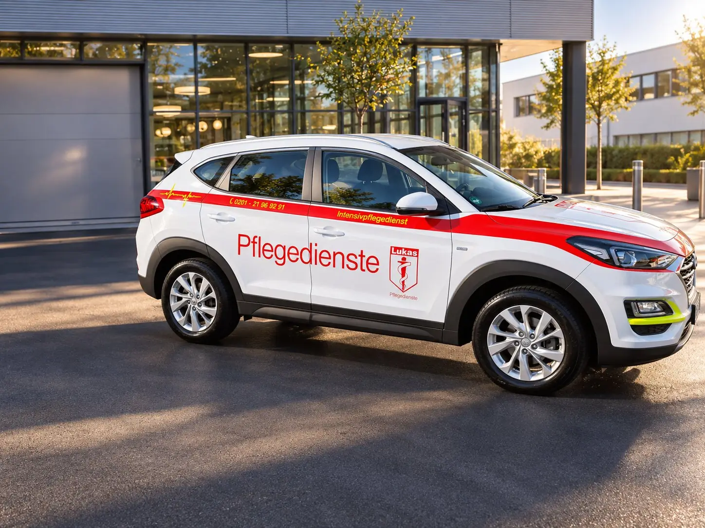 Weiß-rotes Pflegefahrzeug von St. Lukas vor einer Klinik.